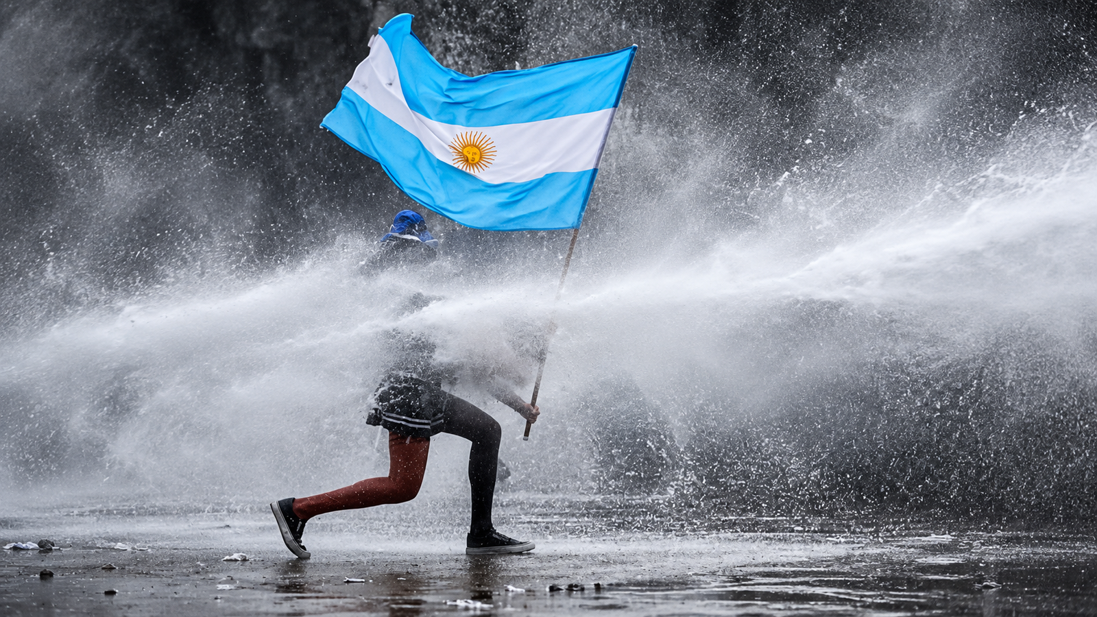Reelaboración editorial con IA: una persona sostiene una bandera argentina mientras resiste un chorro de agua.